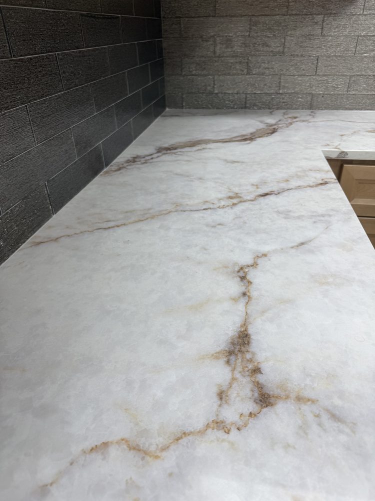 Close-up of a white countertop with copper and brown veining against a dark stacked-stone wall