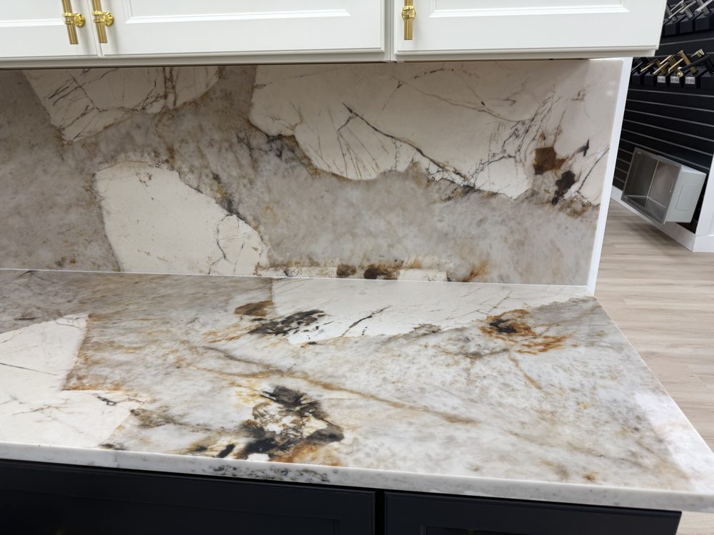 Countertop and matching backsplash in white stone with bold dark and rust-colored markings beneath white shaker cabinets
