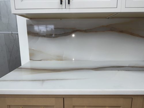 Glossy white countertop with soft gold veining continuing up the wall as a full-height backsplash
