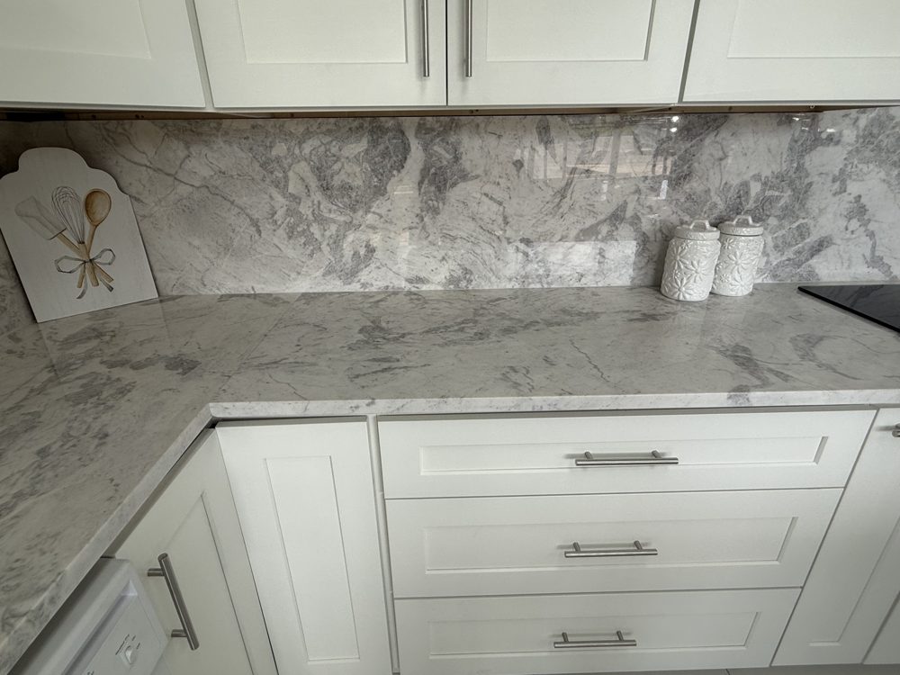 Grey veined stone countertop and backsplash wrapping an L-shaped run of white shaker cabinets