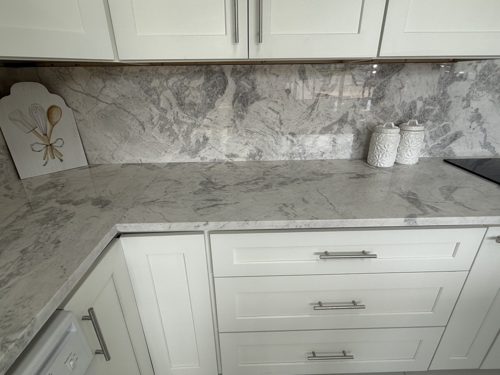 Grey veined stone countertop and backsplash wrapping an L-shaped run of white shaker cabinets