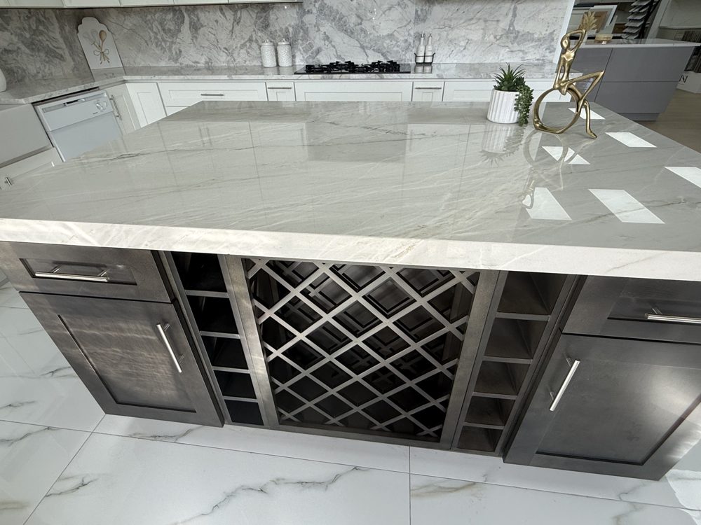 Kitchen island with a polished light grey stone top over dark cabinets and a built-in wine lattice
