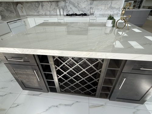 Kitchen island with a polished light grey stone top over dark cabinets and a built-in wine lattice
