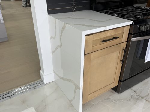 White countertop with grey veining wrapping over a natural maple cabinet as a waterfall edge