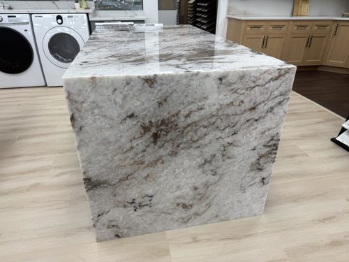 Waterfall island in white stone with brown and grey veining running down both sides to the floor