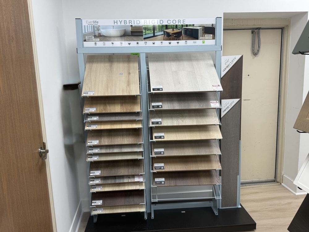 Hybrid rigid core flooring sample rack in the showroom, with rows of wood-look planks in light and medium tones