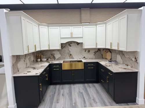 White upper cabinets over navy blue base cabinets, with a gold farmhouse sink and marble backsplash