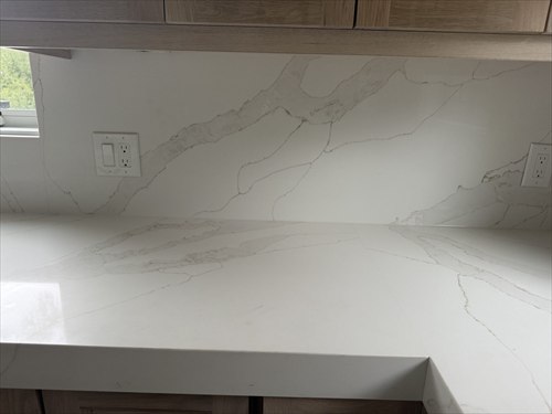 White quartz countertop with soft gold veining continuing up the wall as a full-height backsplash under oak cabinets