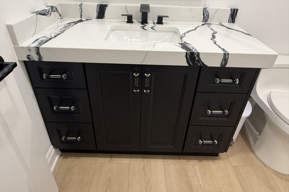 Bathroom vanity with dark raised-panel doors, crystal pulls, and a white countertop with bold black veining
