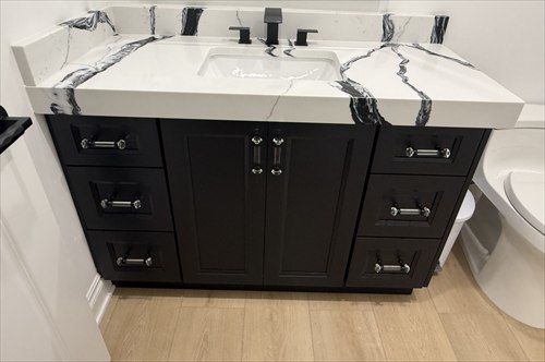 Bathroom vanity with dark raised-panel doors, crystal pulls, and a white countertop with bold black veining
