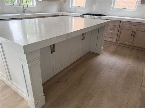 Oversized white island with a thick polished white countertop, decorative legs, and gold pulls beside oak cabinets
