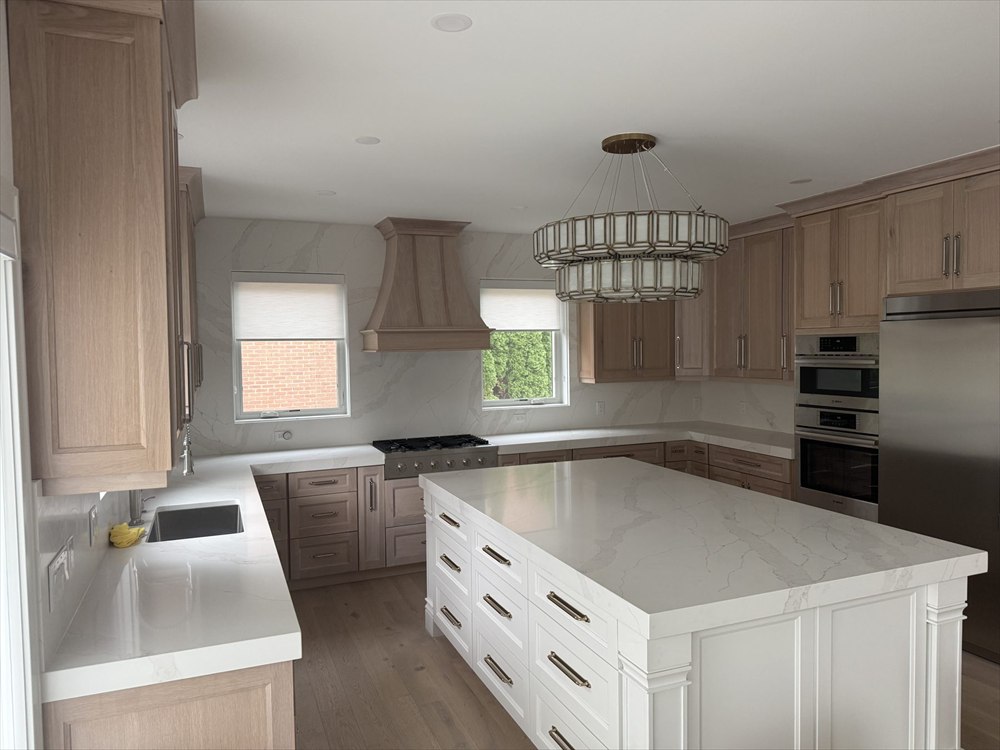 Kitchen with natural oak raised-panel cabinets, a matching wood range hood, a white island with brushed gold pulls, and white veined countertops running up the walls